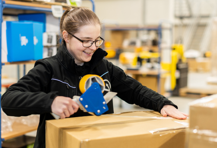 Lachende magazijnmedewerker die een kartonnen doos afsluit met verpakkingstape in een logistieke faciliteit.