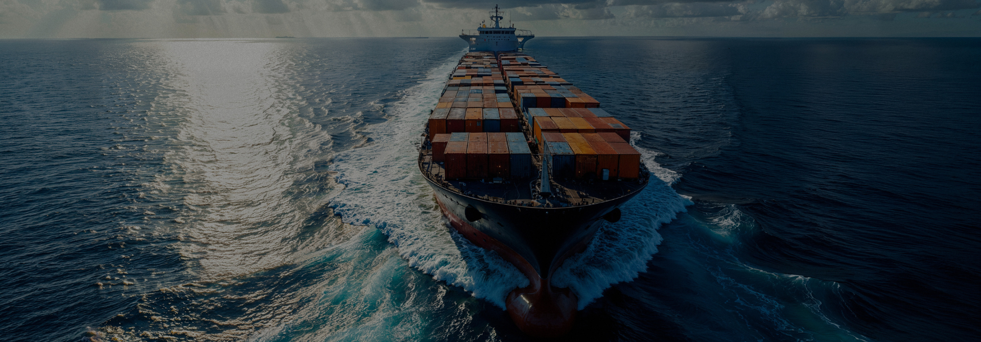 Luchtfoto van een groot containerschip dat over open water vaart en een witte kielzog achterlaat.